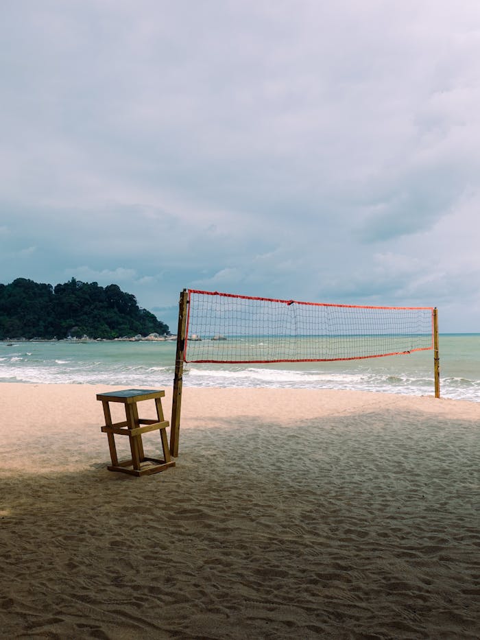A scenic view of an empty beach volleyball court on a sandy shoreline with the sea in the background.